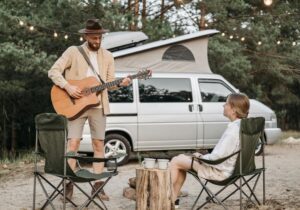 A man playing a guitar outside a campervan, next to a woman