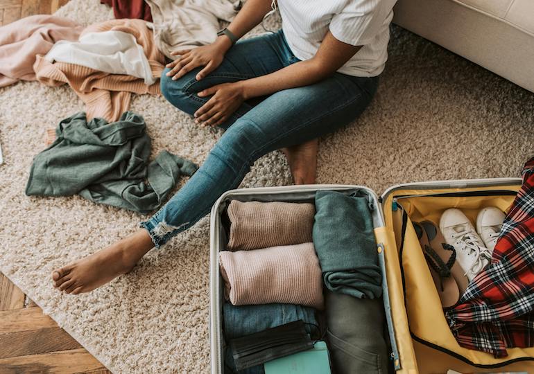 A woman sitting on the floor packing clothes into a suitcase