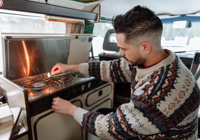 A man in a Christmas jumper lighting the stove in a motorhome